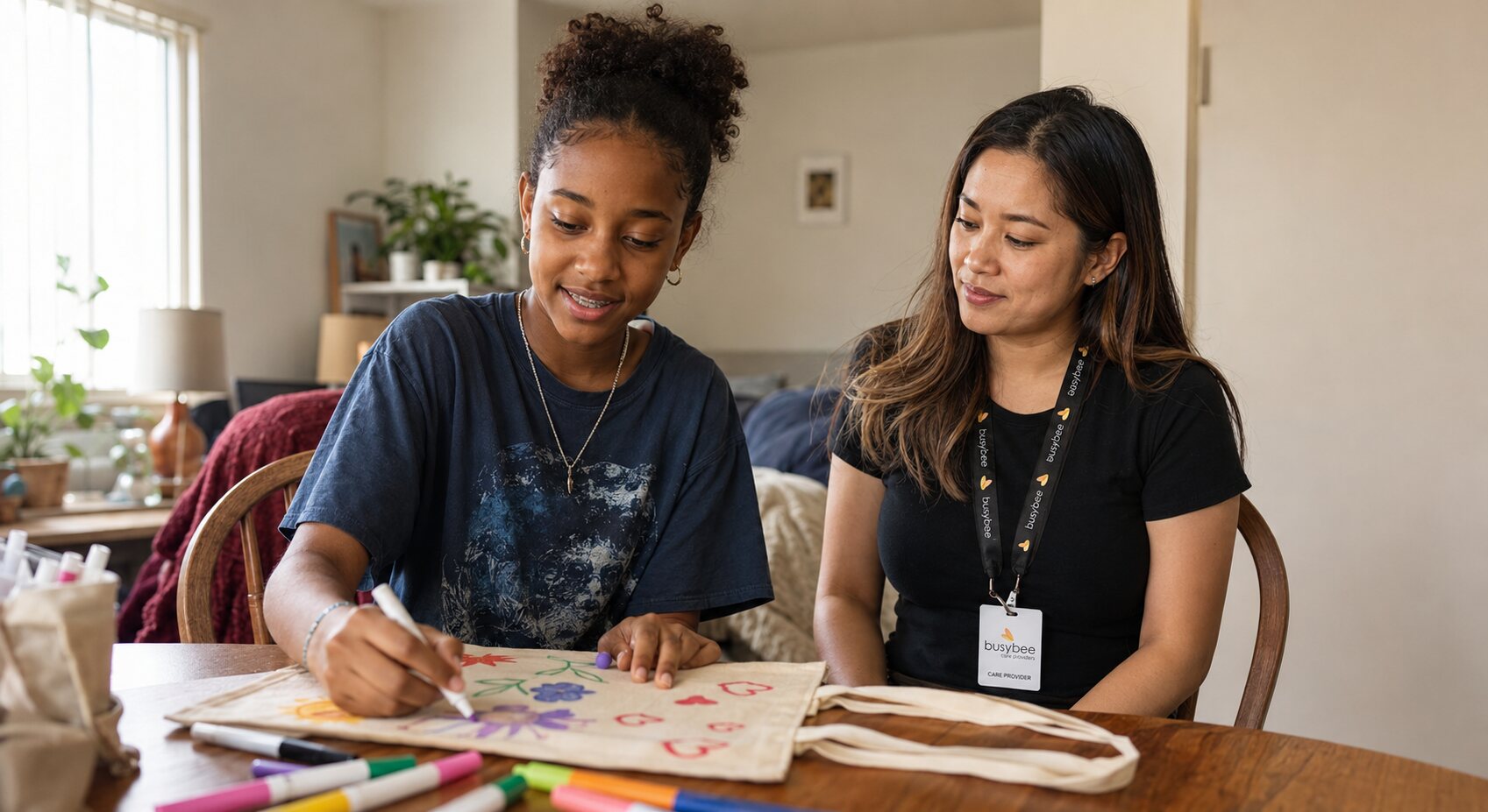 A teenager choosing colors while decorating a tote bag beside a Busy Bee respite provider.
